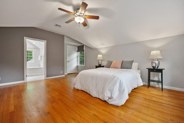 bedroom featuring vaulted ceiling, light wood-style flooring, baseboards, ensuite bath, and ceiling fan