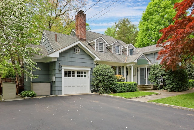 cape cod-style house featuring a shingled roof, a garage, driveway, and a chimney