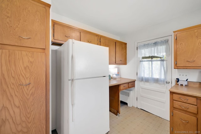 kitchen featuring light countertops, brown cabinetry, radiator heating unit, freestanding refrigerator, and light floors