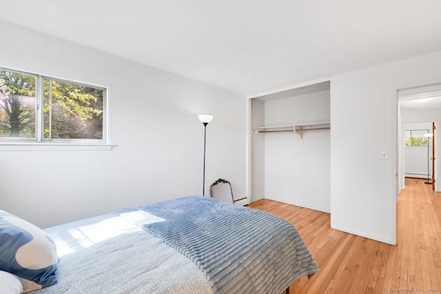 bedroom featuring light wood-type flooring, a baseboard radiator, and a closet
