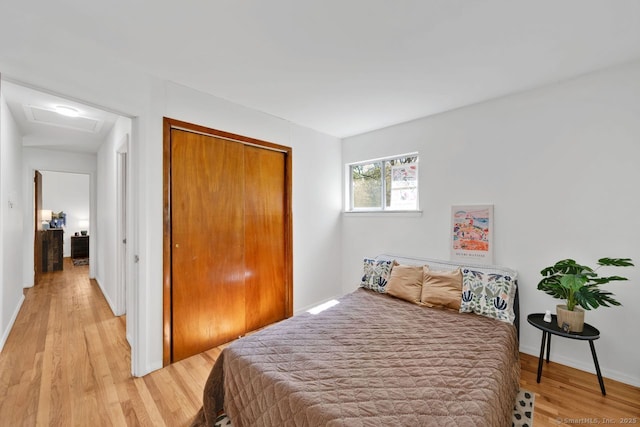 bedroom with a closet, baseboards, attic access, and light wood-type flooring