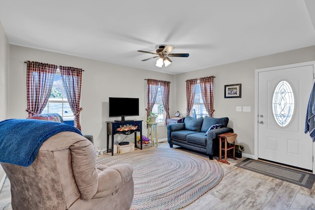 living area with baseboards, light wood-type flooring, and a ceiling fan