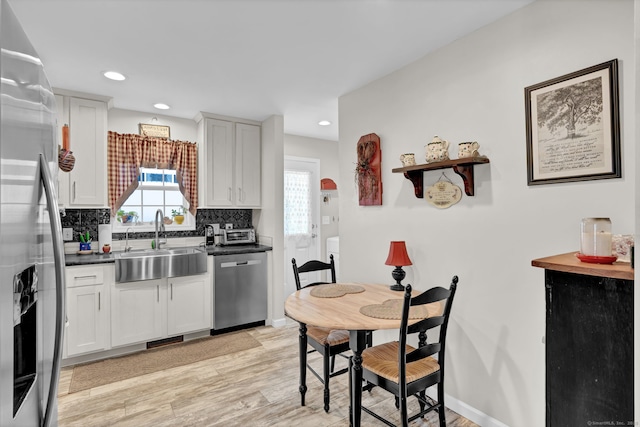 kitchen with light wood-style flooring, appliances with stainless steel finishes, dark countertops, a sink, and white cabinetry