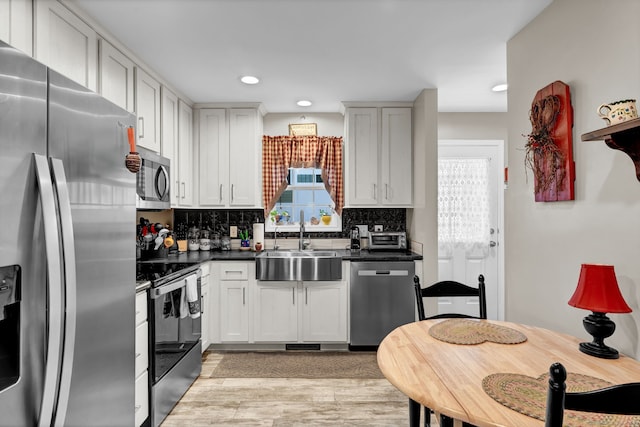 kitchen with a sink, stainless steel appliances, light wood-style flooring, backsplash, and dark countertops