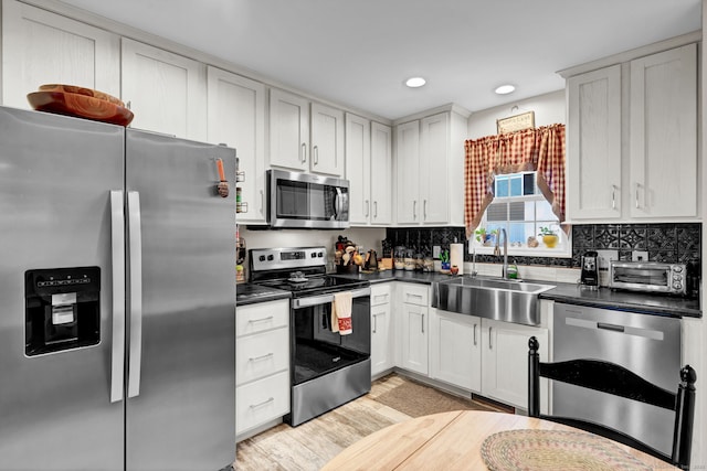 kitchen with a sink, stainless steel appliances, tasteful backsplash, light wood-type flooring, and dark countertops