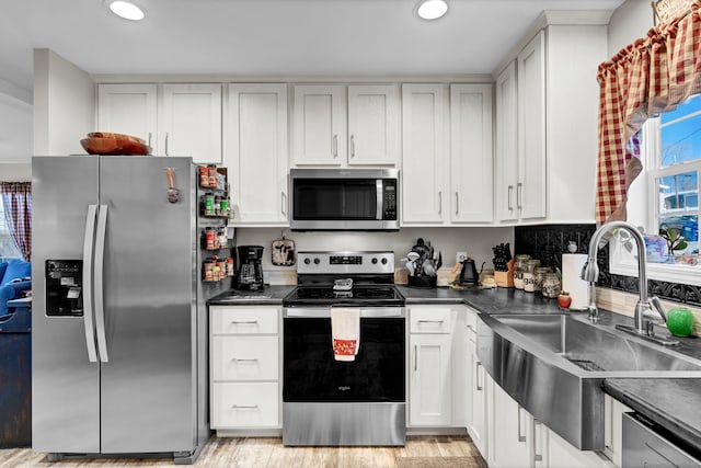 kitchen with dark countertops, stainless steel appliances, white cabinets, and a sink