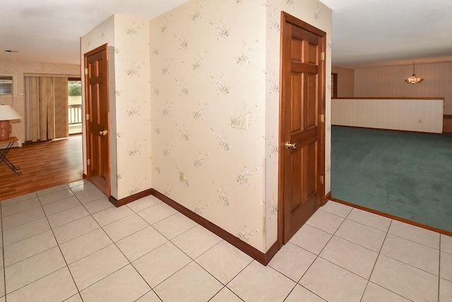 corridor featuring light carpet, wallpapered walls, light tile patterned floors, and baseboards