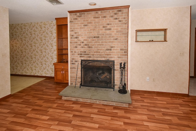 unfurnished living room with wallpapered walls, wood finished floors, a fireplace, and baseboards