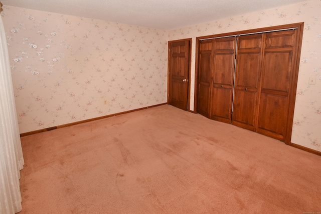 unfurnished bedroom featuring a textured ceiling, wallpapered walls, light colored carpet, and baseboards