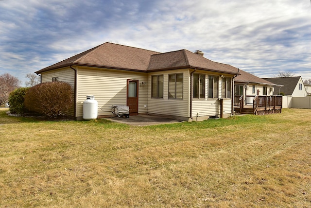rear view of house with a shingled roof, a deck, a yard, a chimney, and a patio