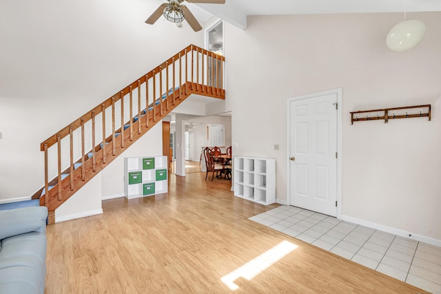 unfurnished living room with high vaulted ceiling, stairs, a ceiling fan, and wood finished floors