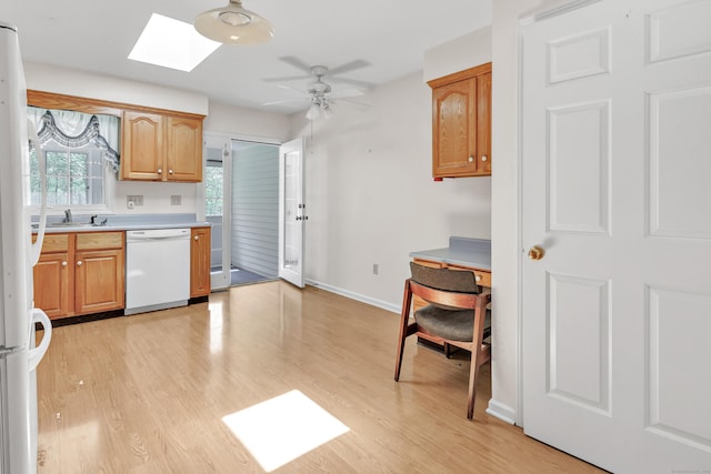 kitchen featuring light wood finished floors, a ceiling fan, a skylight, white appliances, and light countertops
