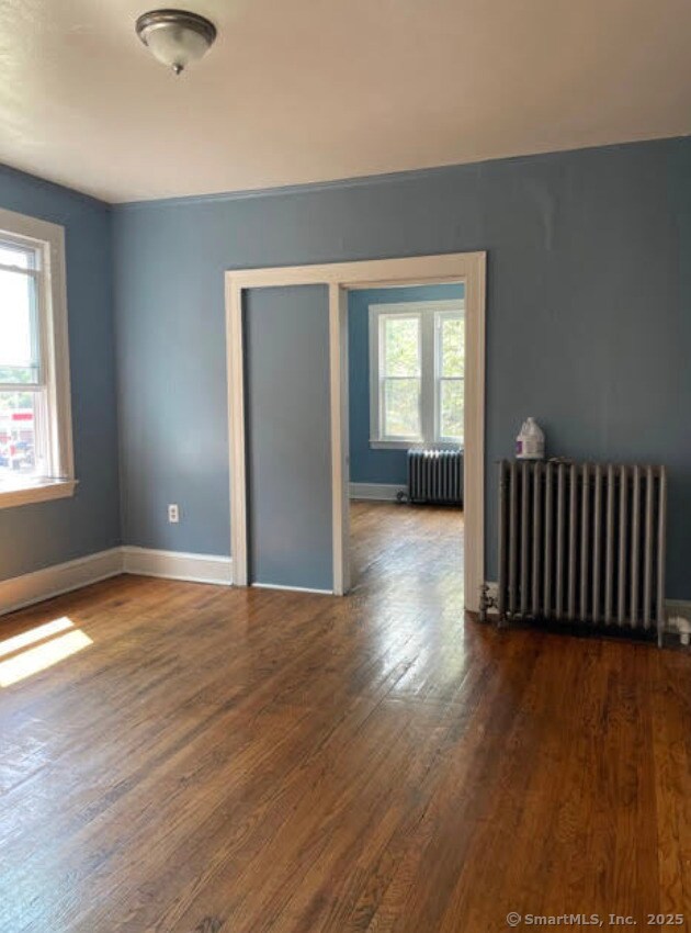 spare room featuring baseboards, wood finished floors, and radiator