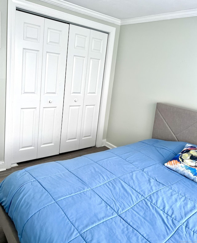 bedroom with baseboards, ornamental molding, a closet, and wood finished floors