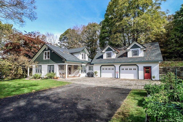 view of front of property with roof with shingles, an attached garage, aphalt driveway, a front lawn, and covered porch