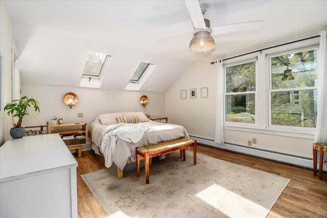bedroom with a ceiling fan, lofted ceiling with skylight, a baseboard heating unit, and wood finished floors