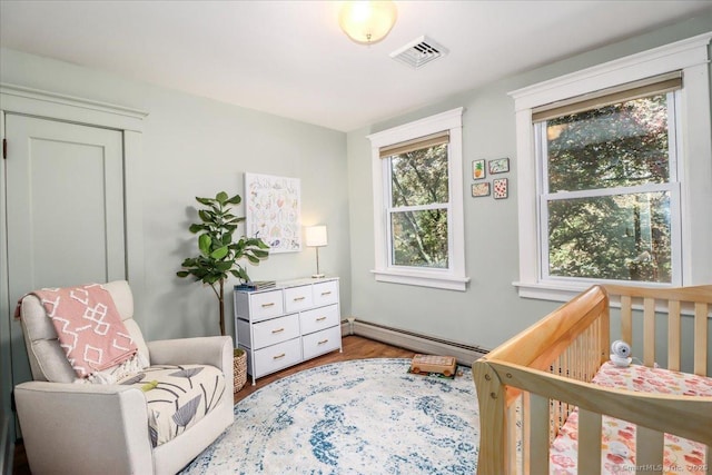 bedroom featuring a baseboard radiator, wood finished floors, a crib, and visible vents