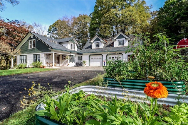 cape cod house featuring a porch, aphalt driveway, and an attached garage
