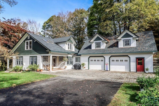 view of front of home with roof with shingles, an attached garage, driveway, a front yard, and a porch