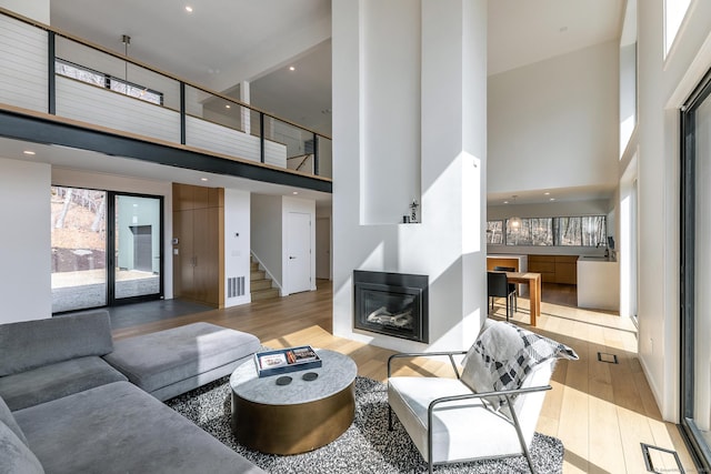 living area featuring a glass covered fireplace, a towering ceiling, wood finished floors, and stairway