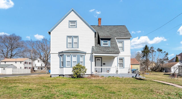 view of front of property featuring a chimney, a front yard, covered porch, and roof with shingles