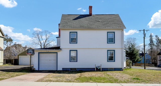 back of house featuring roof with shingles, an attached garage, driveway, a yard, and a chimney