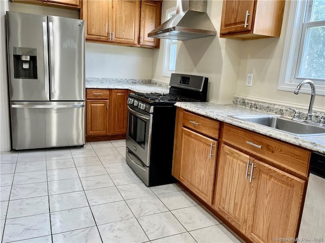 kitchen with wall chimney range hood, brown cabinetry, a sink, and stainless steel appliances