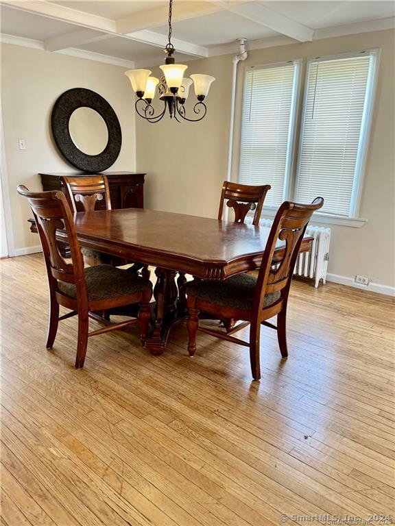 dining area with radiator, an inviting chandelier, baseboards, light wood-style floors, and beamed ceiling