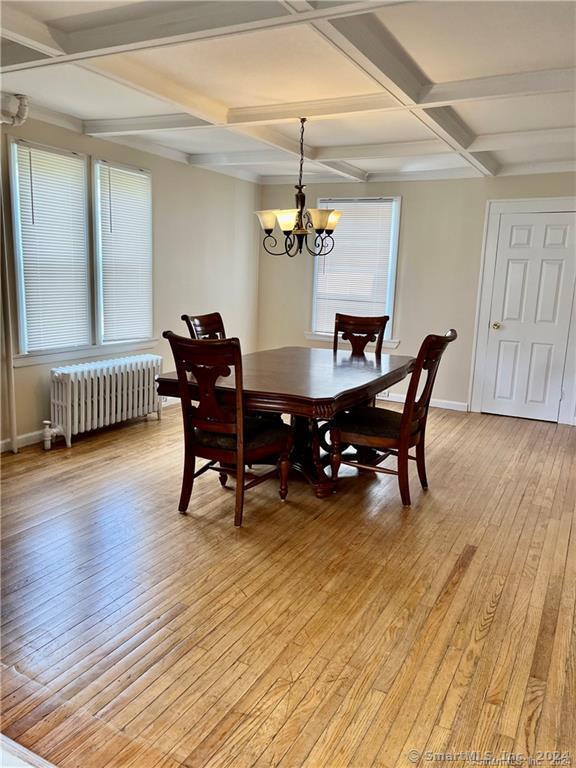 dining room with light wood finished floors, radiator, a notable chandelier, and coffered ceiling