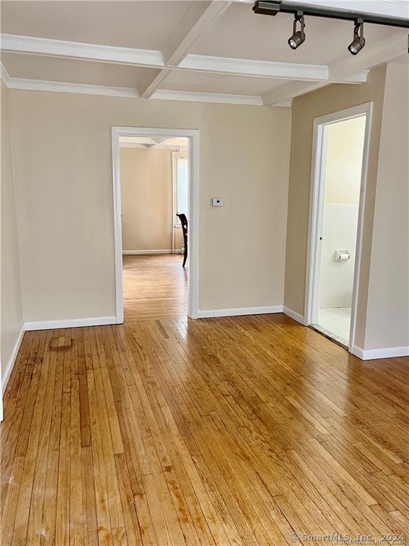 spare room featuring baseboards, light wood-style floors, beam ceiling, and rail lighting