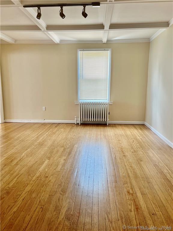 empty room featuring hardwood / wood-style flooring, baseboards, beamed ceiling, and radiator