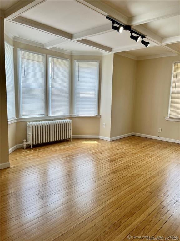 empty room with coffered ceiling, wood-type flooring, baseboards, beam ceiling, and radiator heating unit