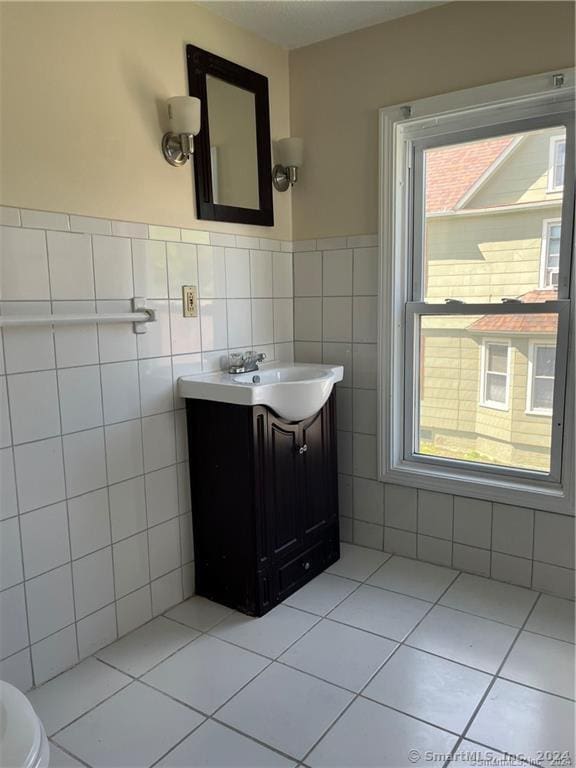 half bathroom with tile patterned floors, wainscoting, vanity, and tile walls