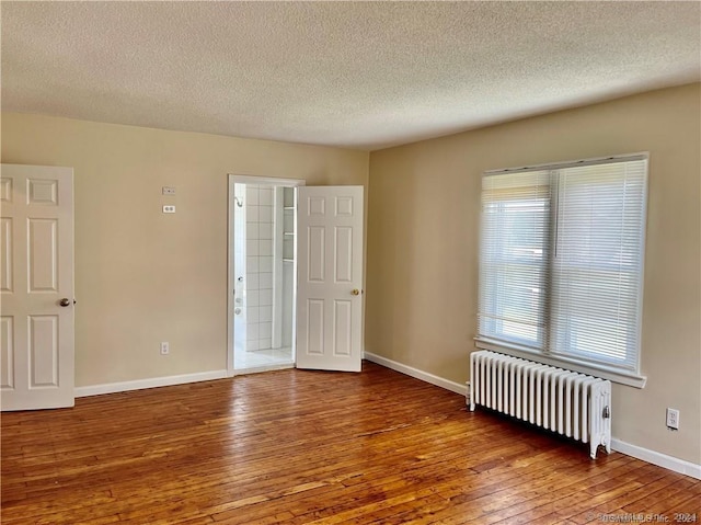 unfurnished room featuring wood-type flooring, a textured ceiling, baseboards, and radiator