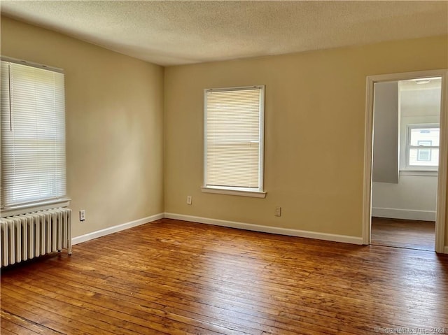 unfurnished room featuring baseboards, radiator heating unit, and hardwood / wood-style flooring