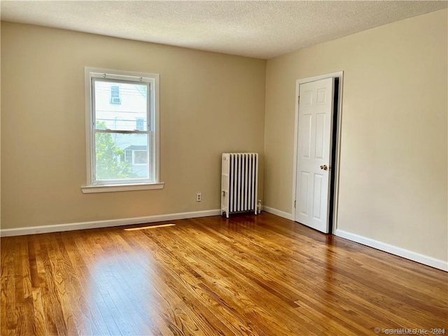 unfurnished room featuring baseboards, a textured ceiling, wood finished floors, and radiator heating unit