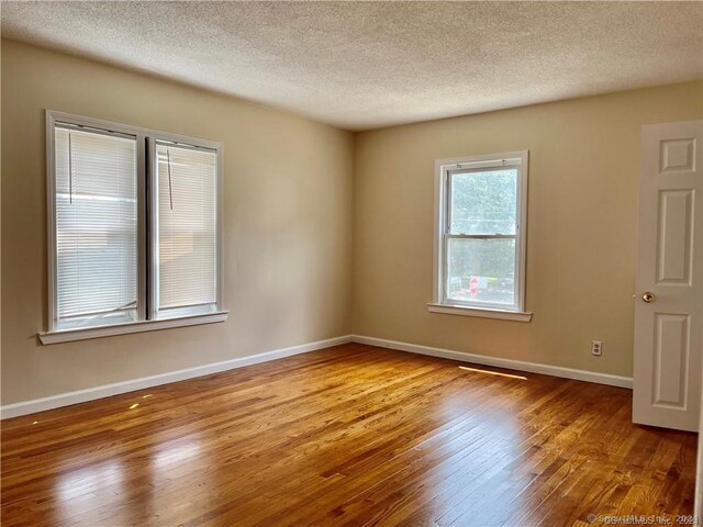 spare room with a textured ceiling, baseboards, and wood finished floors