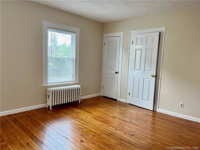 unfurnished bedroom with radiator, light wood-style flooring, and baseboards