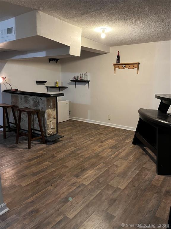 interior space featuring a bar, visible vents, a textured ceiling, and wood finished floors
