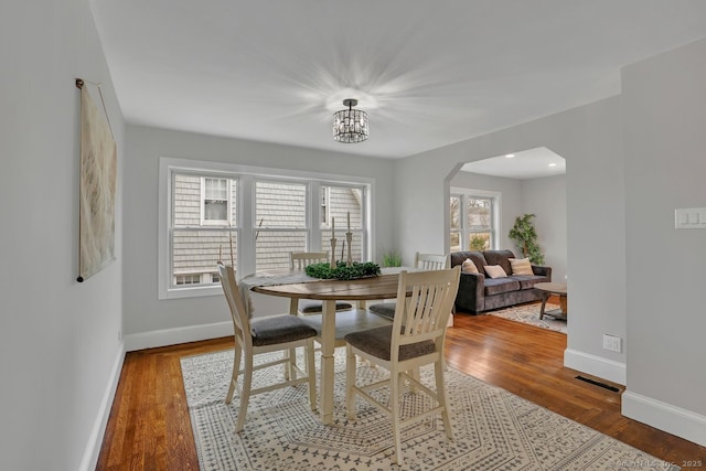 dining area with an inviting chandelier, baseboards, arched walkways, visible vents, and wood finished floors