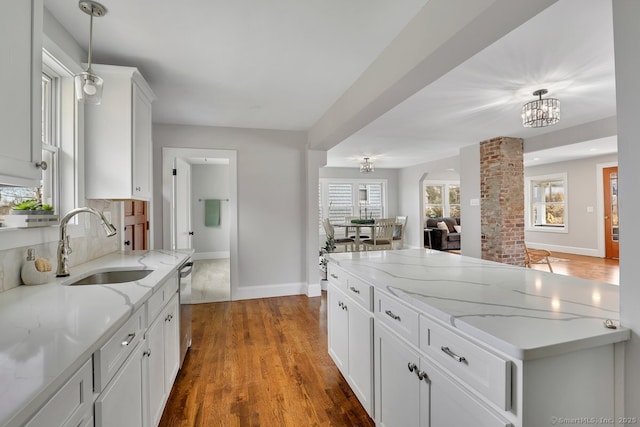 kitchen featuring white cabinets, baseboards, wood finished floors, a sink, and hanging light fixtures