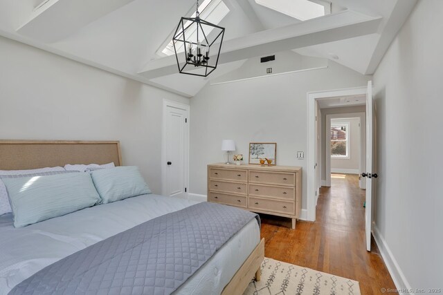 bedroom with baseboards, vaulted ceiling with skylight, wood finished floors, and an inviting chandelier