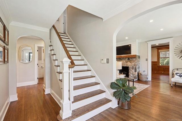 staircase featuring arched walkways, wood finished floors, a fireplace, and ornamental molding