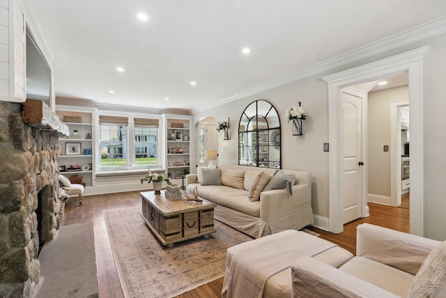 living room featuring crown molding, arched walkways, wood finished floors, baseboards, and recessed lighting
