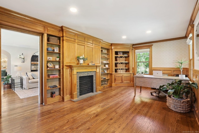 home office featuring crown molding, arched walkways, a wainscoted wall, a fireplace with flush hearth, and light wood finished floors