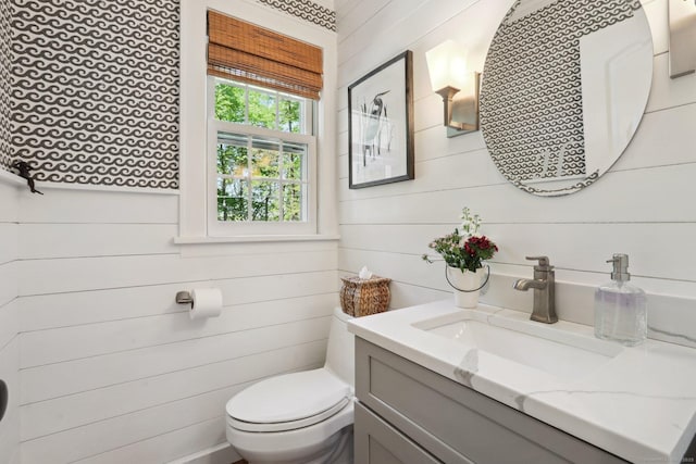 half bath featuring vanity, wood walls, and toilet