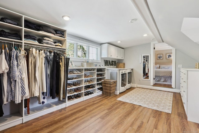spacious closet with separate washer and dryer, light wood-style flooring, and vaulted ceiling