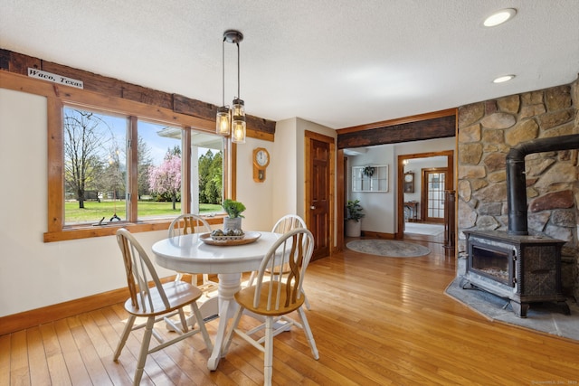 dining area featuring a textured ceiling, baseboards, light wood-style flooring, and a wood stove