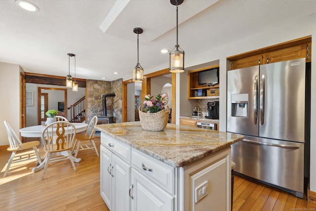 kitchen featuring stainless steel fridge with ice dispenser, a kitchen island, light wood-type flooring, and decorative light fixtures