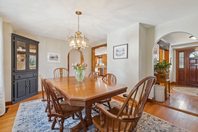 dining area featuring arched walkways, baseboards, an inviting chandelier, and light wood-type flooring